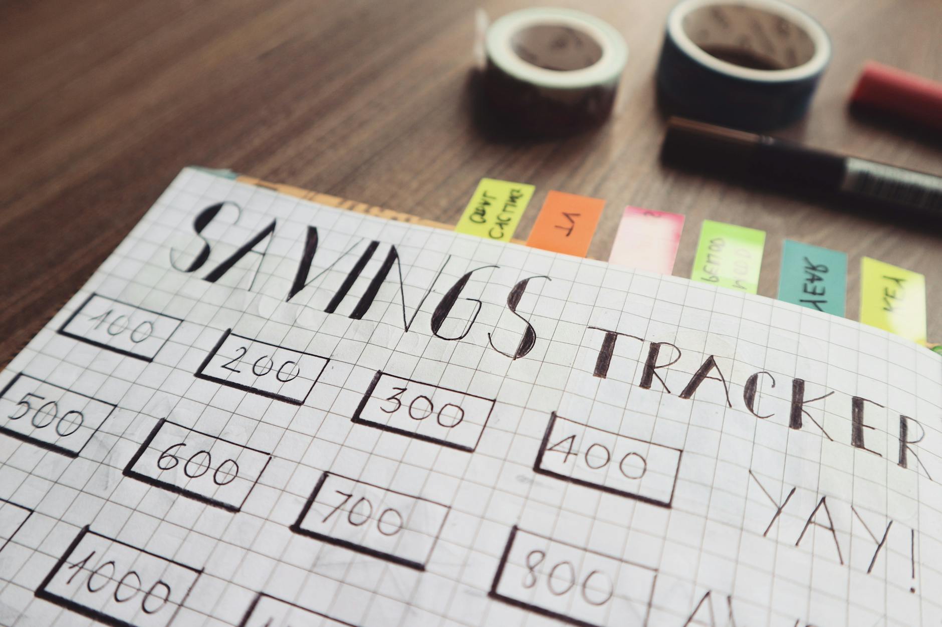 A hand-drawn "Savings Tracker" page in a notebook with colored tabs — a visual aid for setting aside a fixed share of income